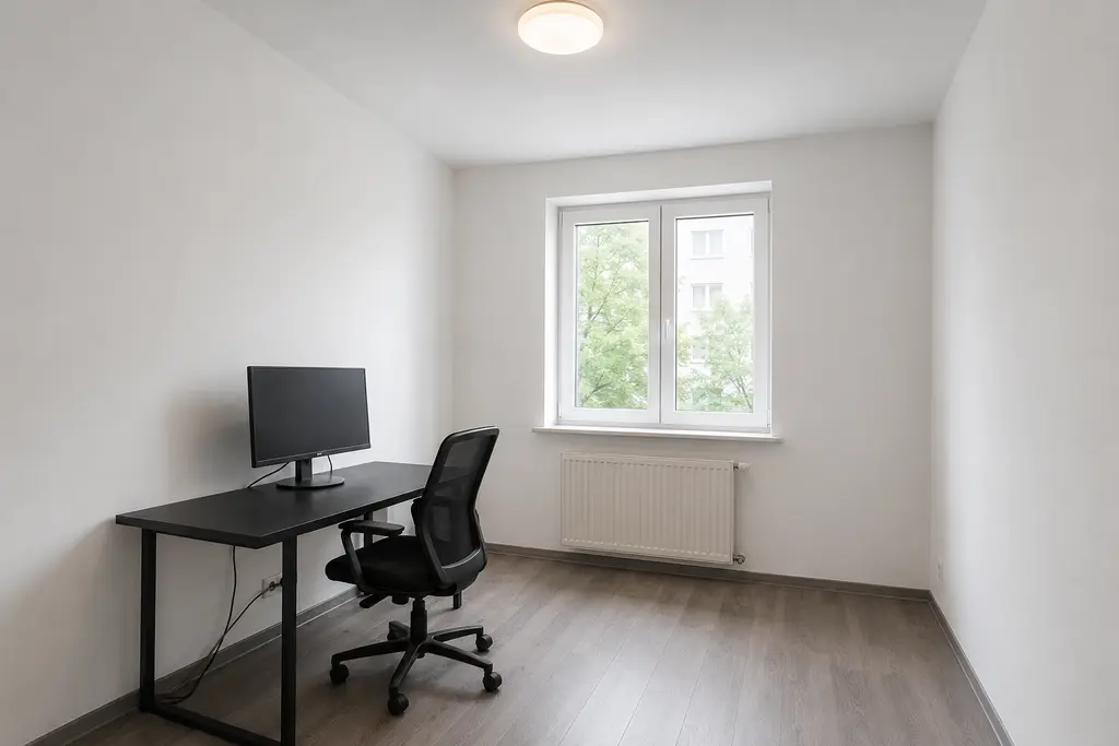 Basic gaming room before the interior design transformation, with white walls, a black desk, monitor and overhead light.