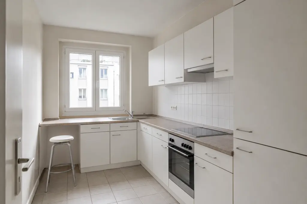 Compact kitchen before the interior design transformation, with white laminate cabinets, a tiled backsplash and flat daylight.