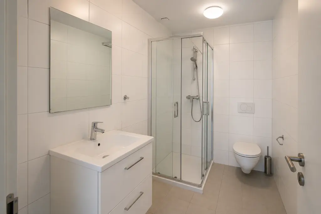 Plain bathroom before the interior design transformation, with white tiles, a standard vanity, mirror and ceiling light.