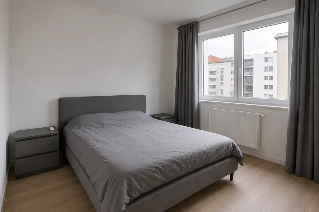 Plain bedroom before the interior design transformation, with white walls, a gray bed and flat natural daylight.